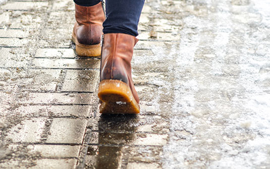 Eine Person, die Schneestiefel trägt und auf einem vereisten Bürgersteig geht Eine Person, die Schneestiefel trägt und auf einem vereisten Bürgersteig geht