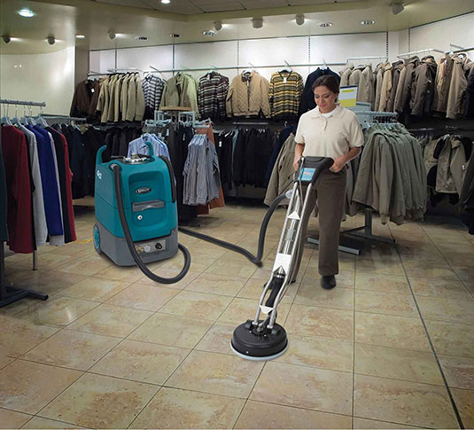un equipo de mantenimiento limpia los azulejos en una tienda de ropa usando la máquina de limpieza para superficies múltiples Tennant Q12 un equipo de mantenimiento limpia los azulejos en una tienda de ropa usando la máquina de limpieza para superficies múltiples Tennant Q12