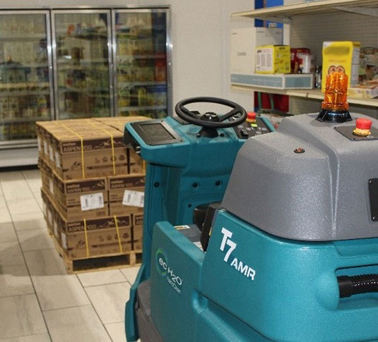 A máquina robótica de limpeza de pavimentos T7AMR Tennant a utilizar a inteligência artificial e sensores inteligentes para contornar uma palete de alimentos numa mercearia. A máquina robótica de limpeza de pavimentos T7AMR Tennant a utilizar a inteligência artificial e sensores inteligentes para contornar uma palete de alimentos numa mercearia.